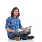 Young male IT professional sitting on the ground with a laptop, smiling