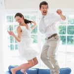 Young couple jumping up and down on a blue couch in ecstasy