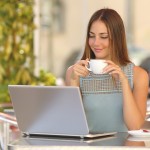Young, self-employed woman sipping coffee and working on a laptop