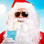 Santa in sunglasses on a beach and drinking a blue cocktail