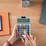 Woman holding and pressing calculator to calculate income expenses and plans for spending money on home loan.