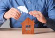 man holding umbrella over a wooden house model depicting protection by lenders mortgage insurance against default