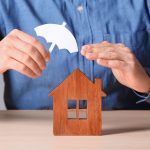 man holding umbrella over a wooden house model depicting protection by lenders mortgage insurance against default