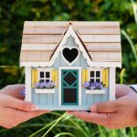 Two people holding a model of a house