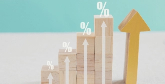 Wooden blocks arranged in a staircase pattern with white percentage symbols and upward arrows, representing a rise in interest rates or growth metrics.