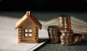  A small wooden house model with stacks of coins next to paperwork.  