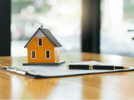 A miniature house on top of a clipboard with a pen