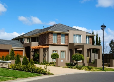 A two-storey modern house with a mix of brick and beige cladding, featuring large windows and a well-maintained garden. The property has a driveway, lush greenery, and a pergola at the entrance, exuding a contemporary and inviting look.