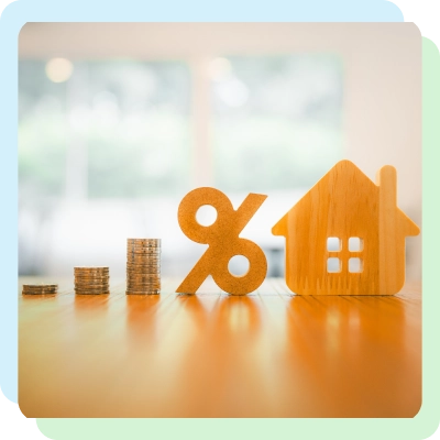 Wooden percentage sign and house model next to stacked coins on a table, symbolizing interest rates and home financing.