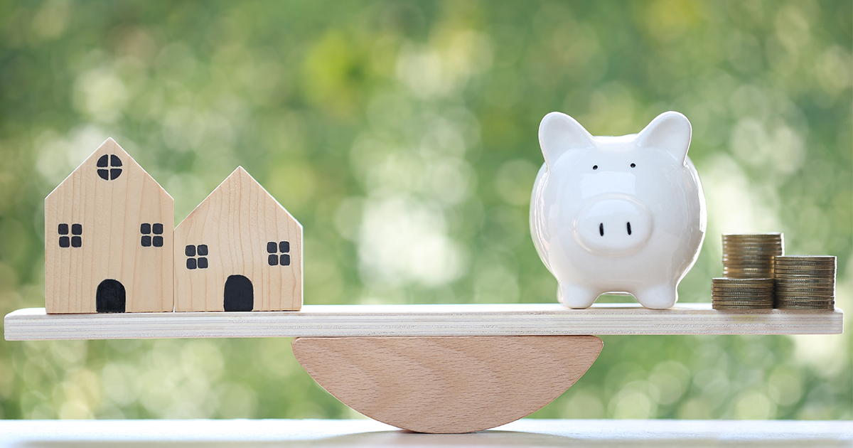 Scale with houses on one side and piggy bank with coins on the other, showing financial balance.