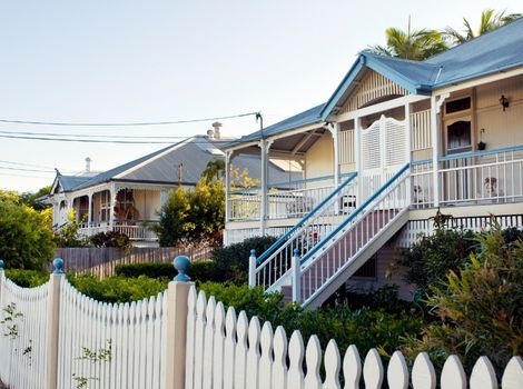 A row of houses in Brisbane, Queensland. The houses have a white fence, and blue roofs.