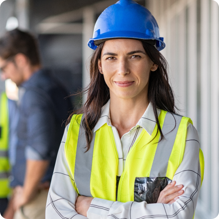 A woman wearing a hard hat and high-visibility vest stands outdoors, indicative of her role in construction or engineering.