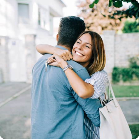 A man and woman embracing outdoors, both smiling and looking happy, embodying a moment of love and affection.