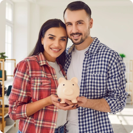 A couple stands together in a bright room, holding a light pink piggy bank, symbolizing savings and future planning.