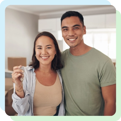 A couple stands together in a bright, modern kitchen, the woman holding keys, suggesting they are celebrating a new home.