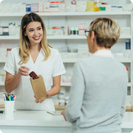 Pharmacist handing medication in a paper bag to a customer at a pharmacy counter