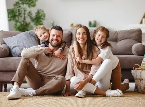 Family of four smiling together while sitting on the living room floor.
