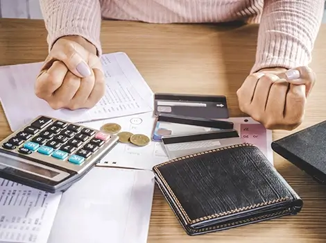 Person with clenched fists at a desk with bills, a calculator, credit cards and a wallet.